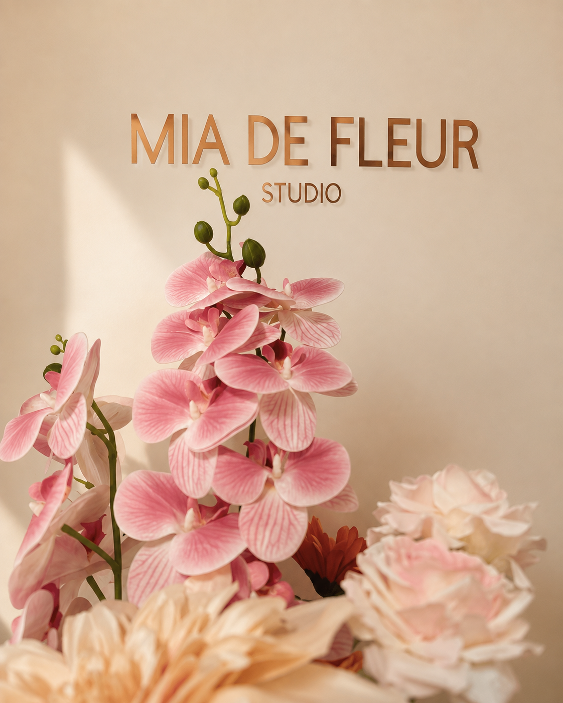 Zlatni natpis Mia De Fleur Studio na bež zidu s roza orhidejama